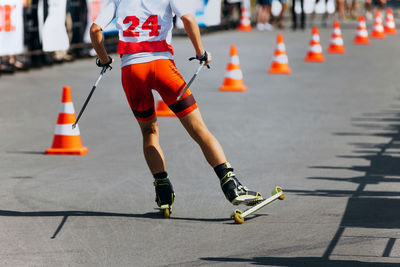 Back athlete skier roller skiing race on asphalt with traffic cone