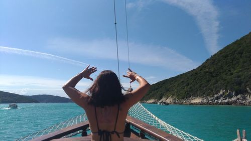 Rear view of woman gesturing on boat in sea against blue sky