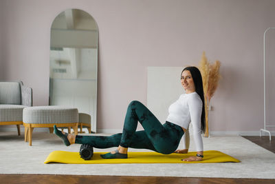 Young woman in sportswear performs a myofascial massage of the lower leg muscles using a roller