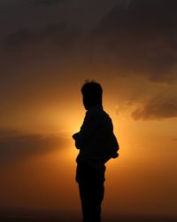 Silhouette boy standing by sea against sky during sunset