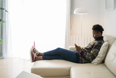 Young woman using smart phone while sitting on sofa in living room