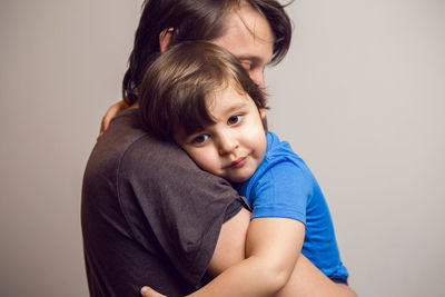 Father in the gray shirt holding a son in a blue t-shirt in the hands of a white wall