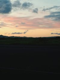 Scenic view of landscape against cloudy sky at sunset