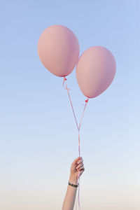 Low angle view of woman holding pink helium balloons against sky