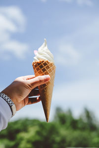 Midsection of person holding ice cream against sky