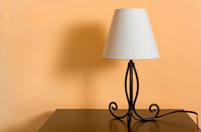 Close-up of electric lamp on table against wall at home