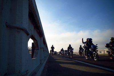 People riding bicycle on road against sky