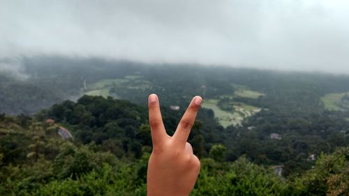 Cropped image of hand gesturing against green landscape