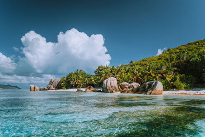 People relaxing on rocks by sea against sky