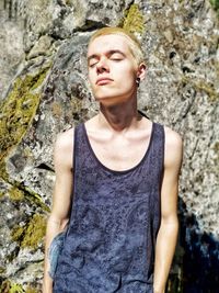 Young man in tank top standing against rock