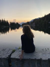 Rear view of woman looking at lake against sky during sunset