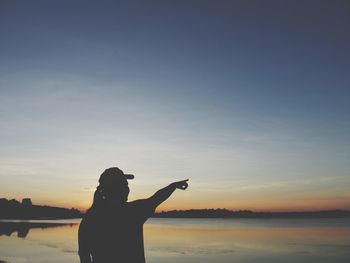 Silhouette woman pointing at sea shore against sky during sunset