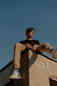 Low angle view of young man looking at camera against clear sky