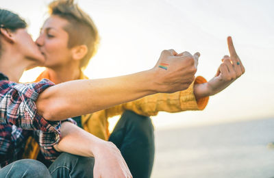 Lesbian couple doing obscene gesture while kissing on mouth