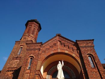 Low single view of church made of red brick and white status against blue sky