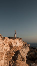 Man on rock by sea against clear sky