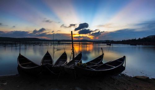 Boat moored at lake against sky during sunset