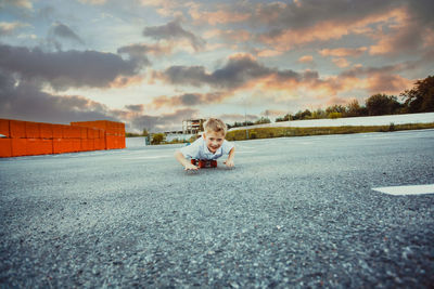 Portrait of boy lying on skateboard against sky