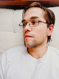 Man wearing eyeglasses looking away while sitting on sofa at home