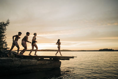 Male and female friends running on jetty towards lake during vacation on sunset