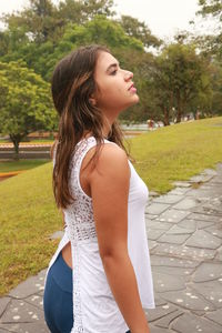 Side view of young woman standing on footpath in public park