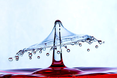 Close-up of drop falling on glass against white background