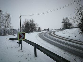 Road sign on snow covered field against sky