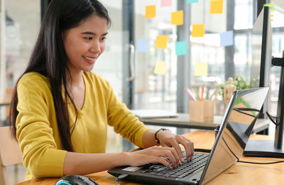 Portrait of smiling woman using phone while sitting on table