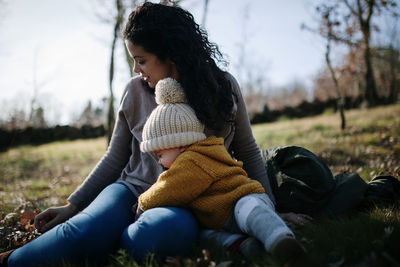 Mother and daughter wearing warm clothing while sitting on land