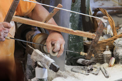 Midsection of craftsperson using hand saw on alabaster at workshop