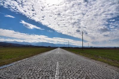 An old stone cube road through a green field and blue cloudy sky