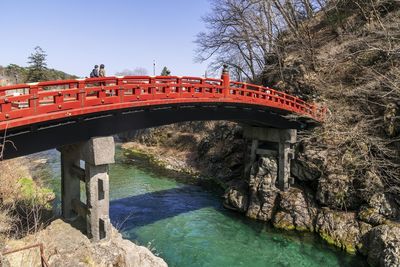Japanese red bridge over river against clear blue sky