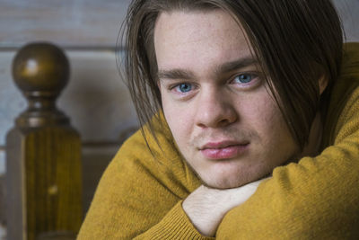 Close-up of young man wearing sweater looking away while leaning on wooden railing at home