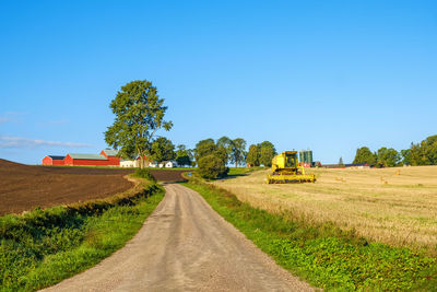 Dirt road amidst field against clear blue sky