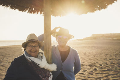 Portrait of happy friends standing at beach against clear sky