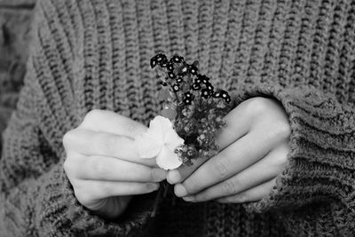 Midsection of person in sweater holding flowers