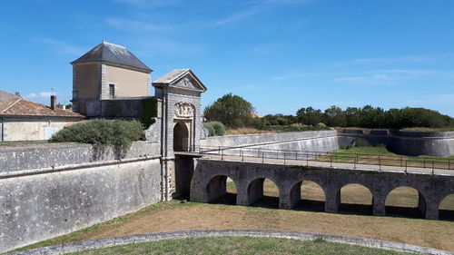 Arch bridge over building by trees against sky