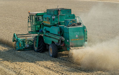 Combine harvester on field against sky at farm during sunset