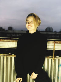 Portrait of smiling woman standing against railing against sky