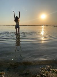 Full length of woman standing on beach against sky during sunset