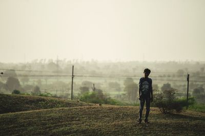 Rear view of man standing on field against sky