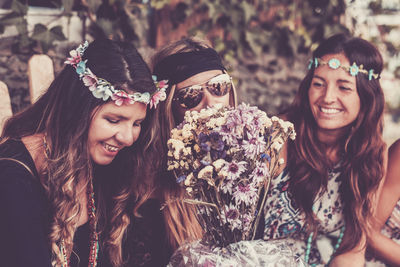 Smiling friends with bouquet sitting in park