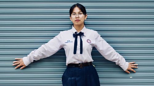 Portrait of young woman in uniform standing against wall