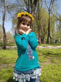 Portrait of smiling cute girl with hands on chin standing on grassy field