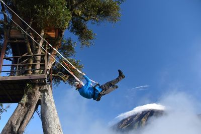 Low angle view of man swinging against blue sky