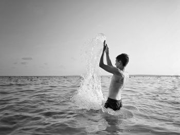 Full length of shirtless man in sea against sky