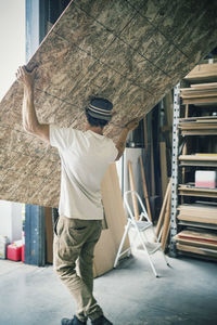 Rear view of carpenter carrying wooden plank at workshop