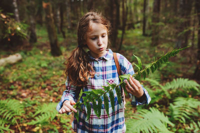 Girl holding plant while standing in forest