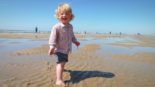 Cheerful boy standing at beach against blue sky