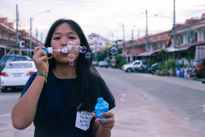 Portrait of girl blowing bubbles on road against sky